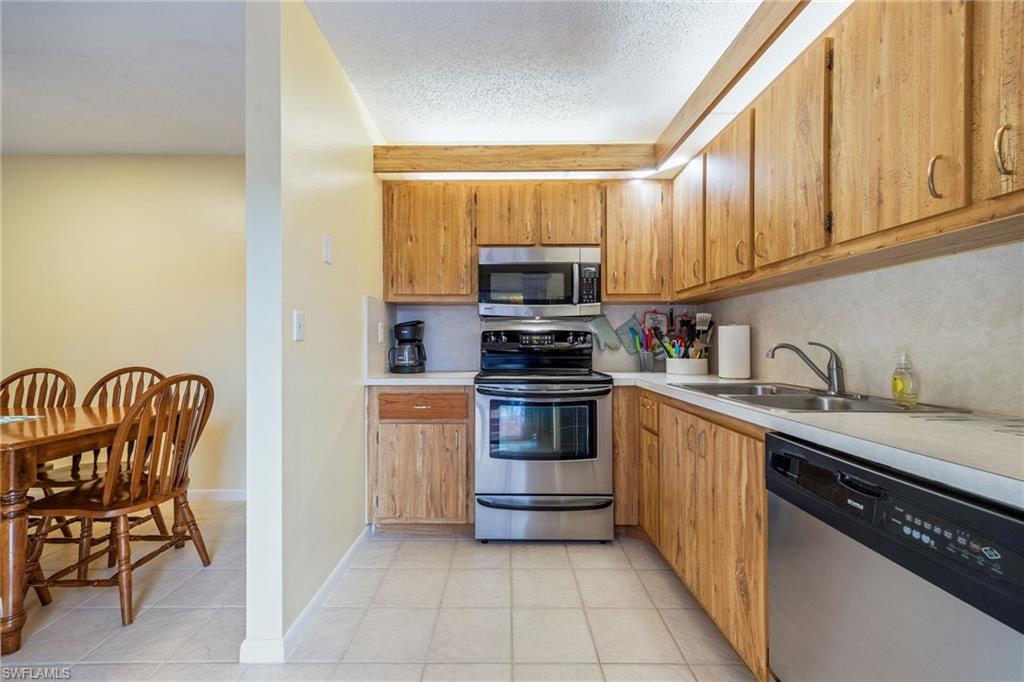Kitchen featuring stainless steel appliances, light countertops, a textured ceiling, light tile patterned flooring, and wood finish cabinetry
