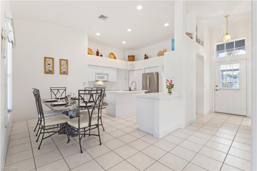 Kitchen featuring a kitchen island, a high ceiling, light countertops, freestanding refrigerator, and white microwave