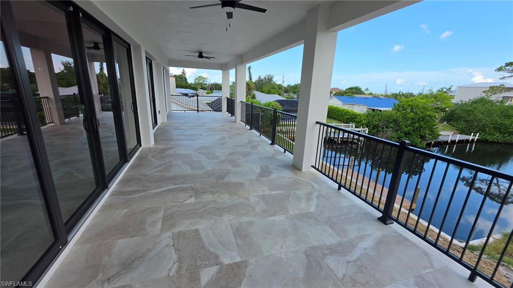 Expansive covered balcony featuring large-format tile flooring, black metal railings, and multiple sliding glass doors