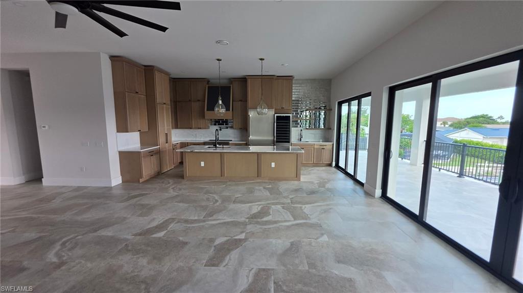Spacious open-concept layout featuring large format tile flooring, a modern kitchen with light wood cabinetry, a center island, and a stainless steel appliance suite