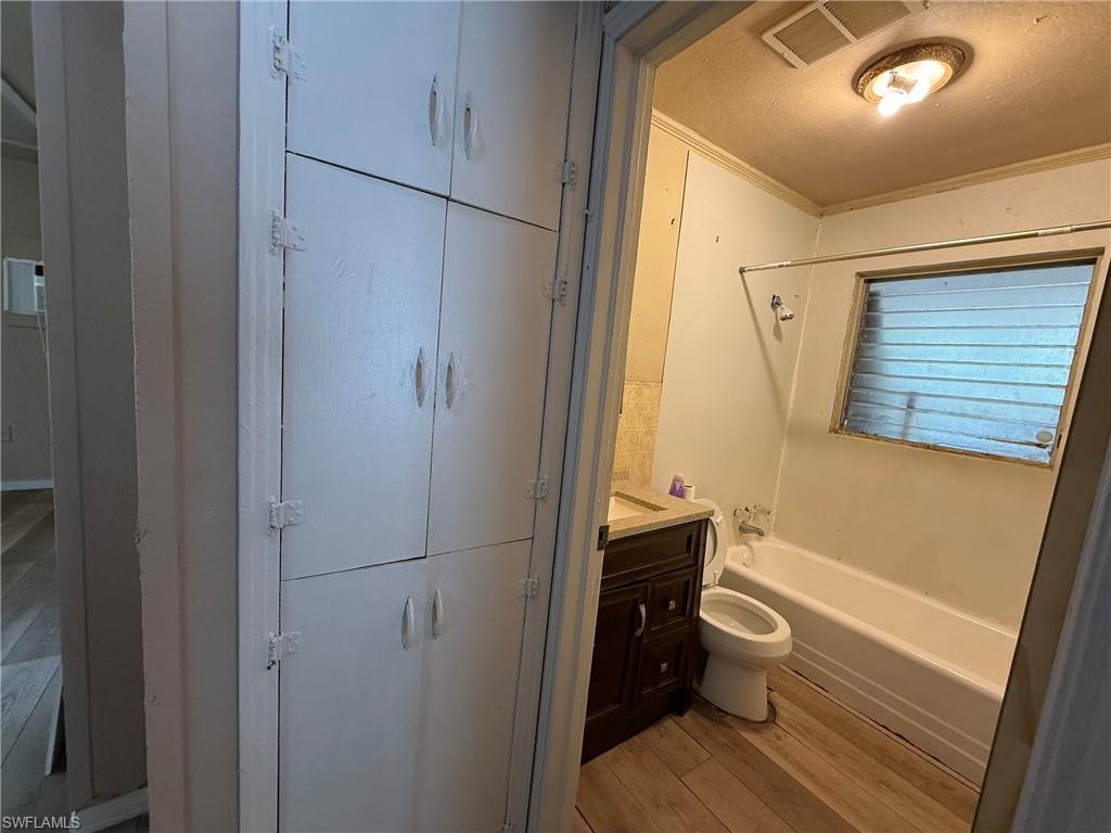 Bathroom with shower / bath combination, vanity, light wood finished floors, ornamental molding, and a textured ceiling