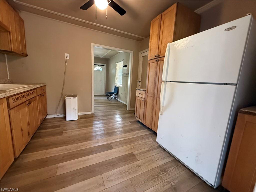 Kitchen featuring freestanding refrigerator, wood finish cabinets, light wood-style floors, ceiling fan, and light countertops
