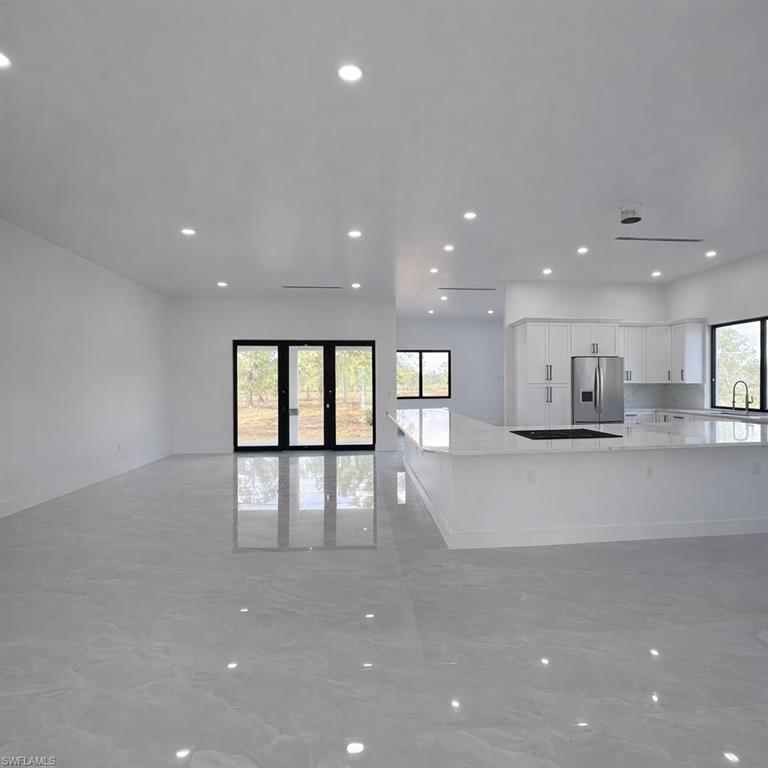 Kitchen with white cabinetry, open floor plan, recessed lighting, light stone countertops, and stainless steel fridge with ice dispenser