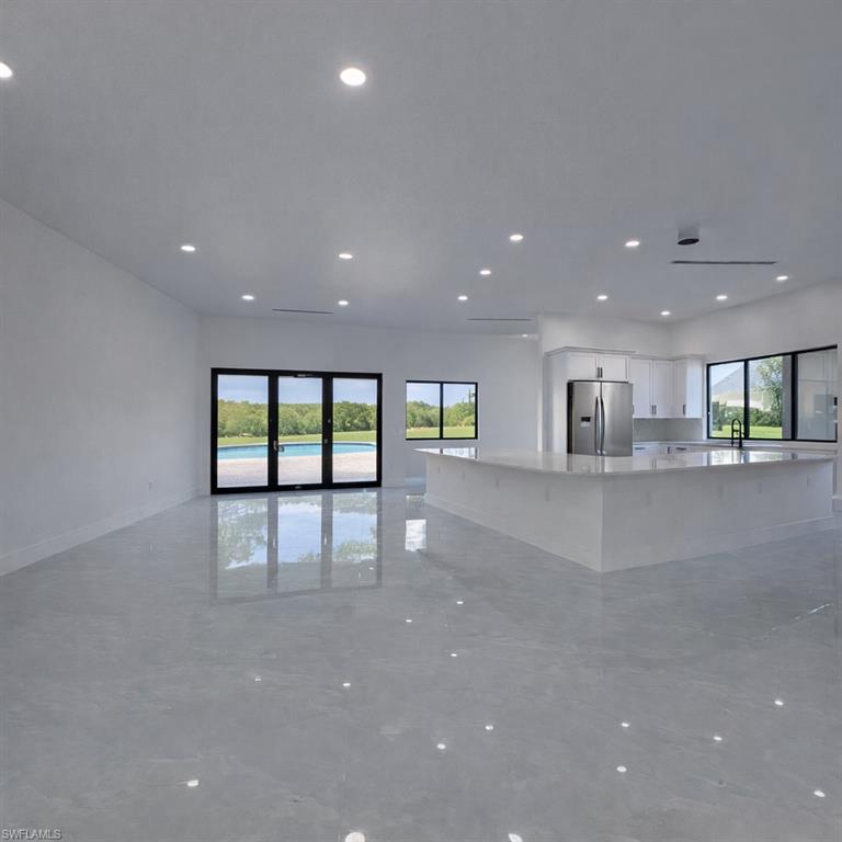 Kitchen with white cabinets, open floor plan, stainless steel fridge with ice dispenser, light stone counters, and a large island