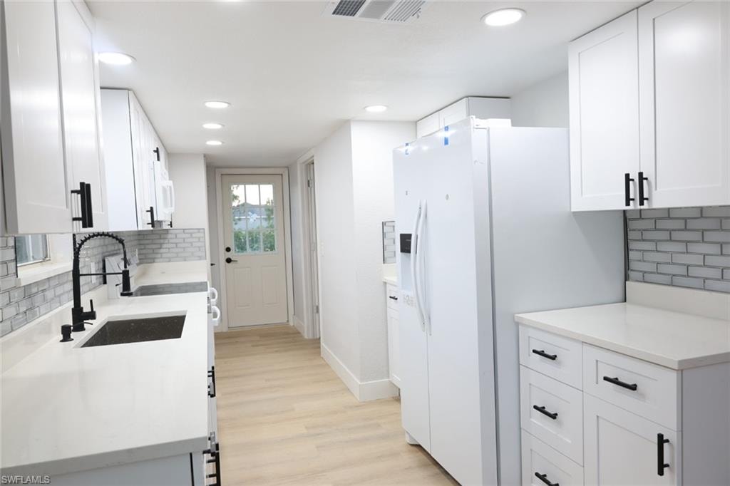Kitchen featuring decorative backsplash, white cabinetry, white fridge with ice dispenser, light wood-style flooring, and recessed lighting