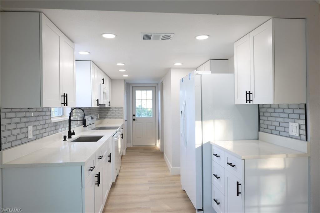 Kitchen featuring backsplash, light stone countertops, white cabinets, and recessed lighting