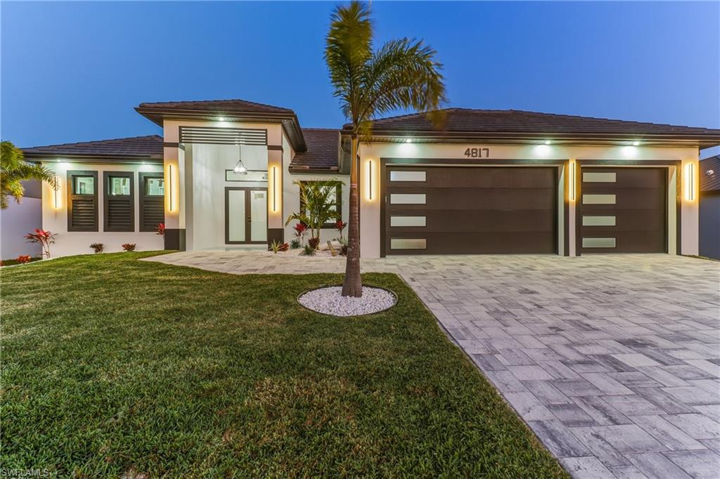 featuring a yard, paver driveway,d 3 car garage