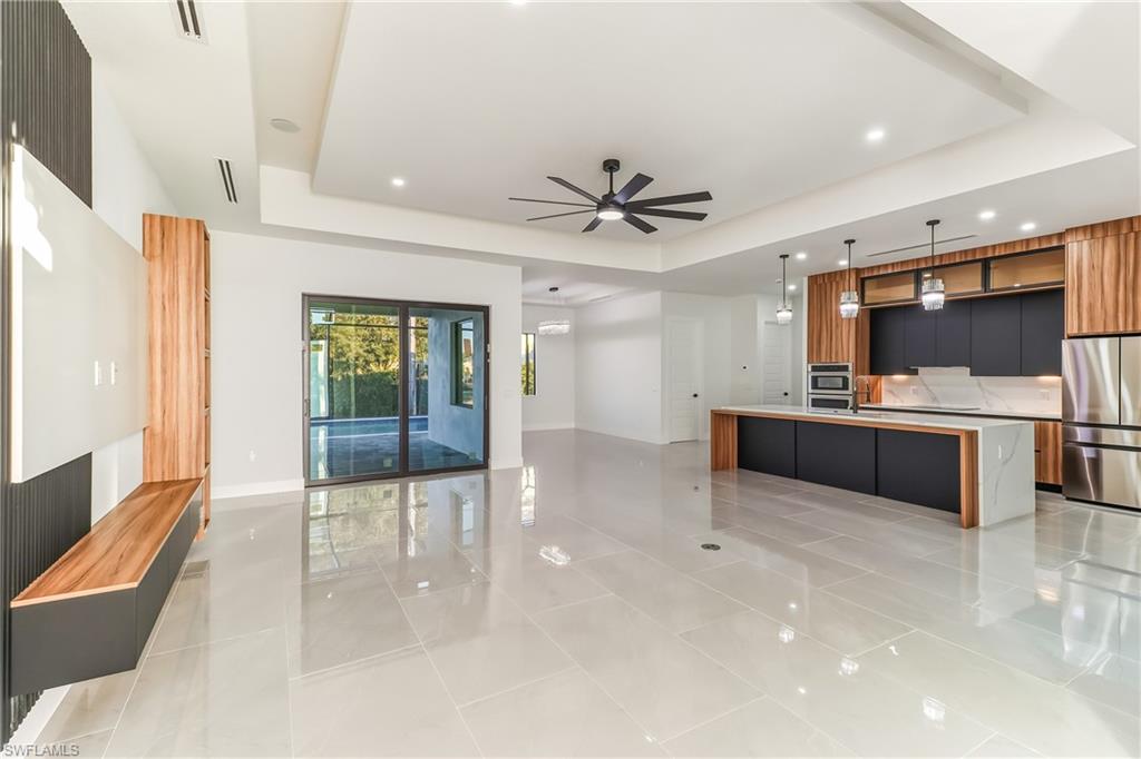 featuring modern cabinets, pendant lighting, open floor plan, freestanding refrigerator, and a large waterfall quartz center island with sink