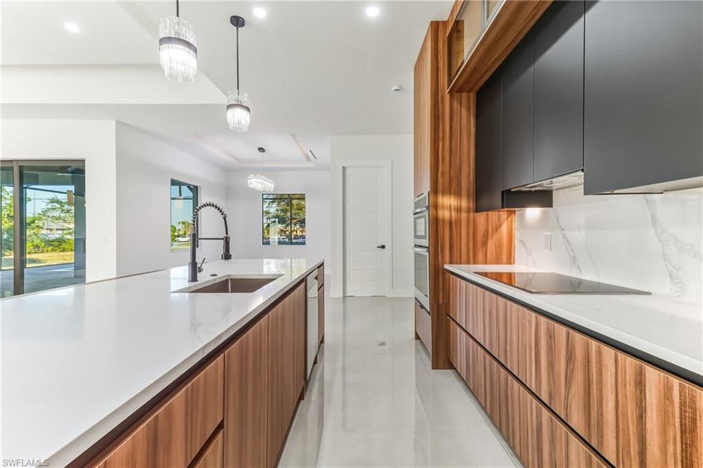 Kitchen featuring modern cabinets, light stone counters, decorative backsplash, light tile patterned floors, and black electric stovetop
