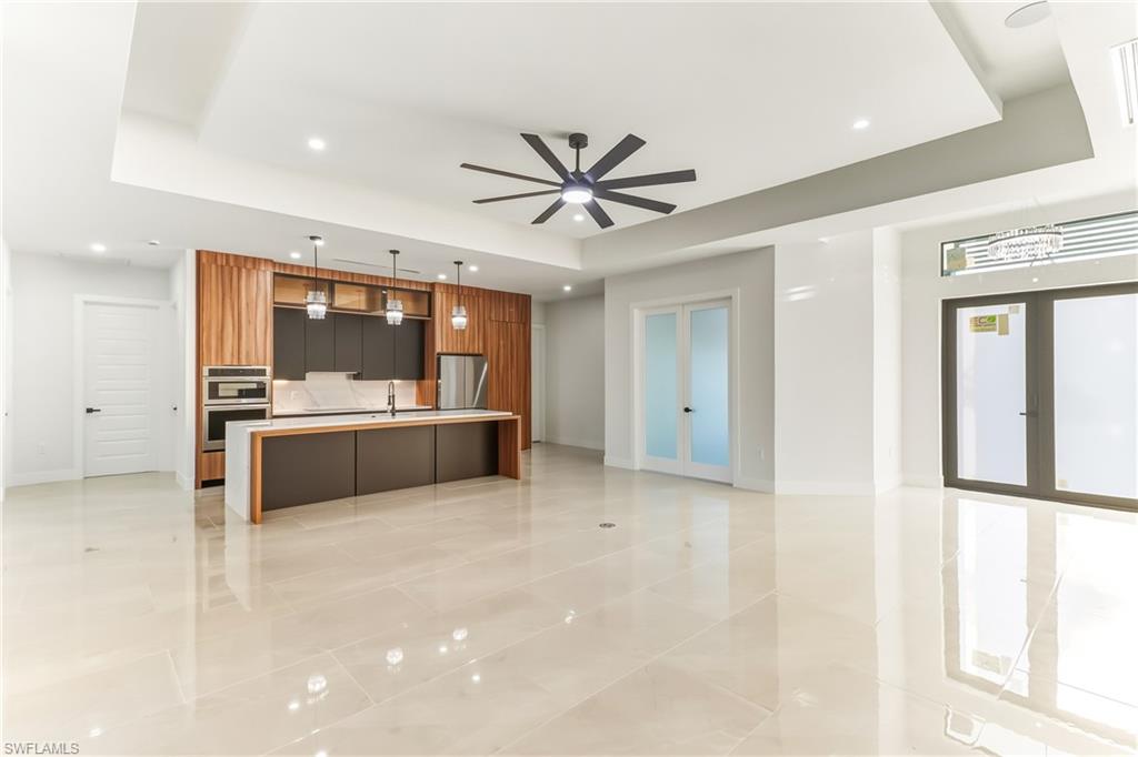 Kitchen with modern cabinets, open floor plan, pendant lighting, center quartz waterfall island with sink and raised ceilings with backlighting.