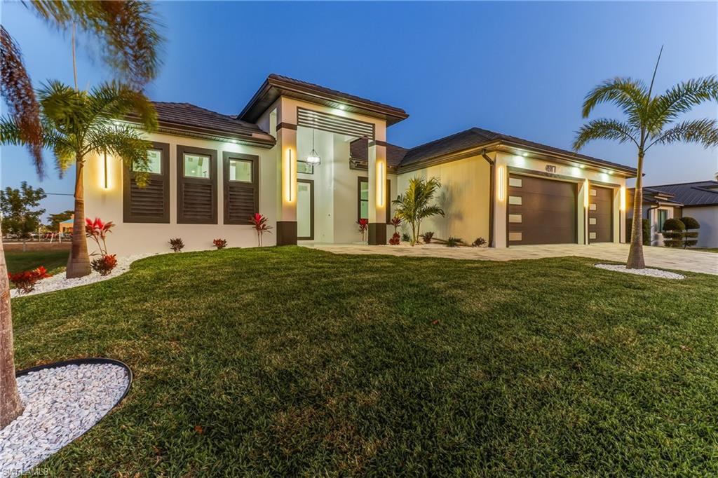 View of front of Modern Luxury pool home with a front yard, Concrete block structure, an attached 3 car garage, and paver driveway