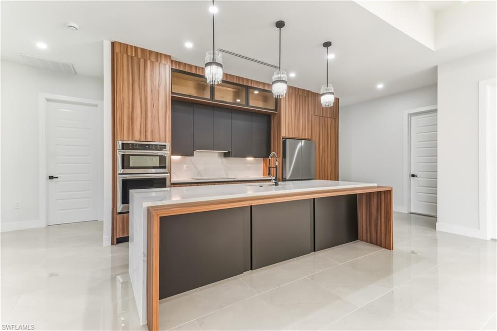 Kitchen featuring modern cabinets, two tone cabinets, a kitchen island with sink, decorative light fixtures, and stainless steel appliances