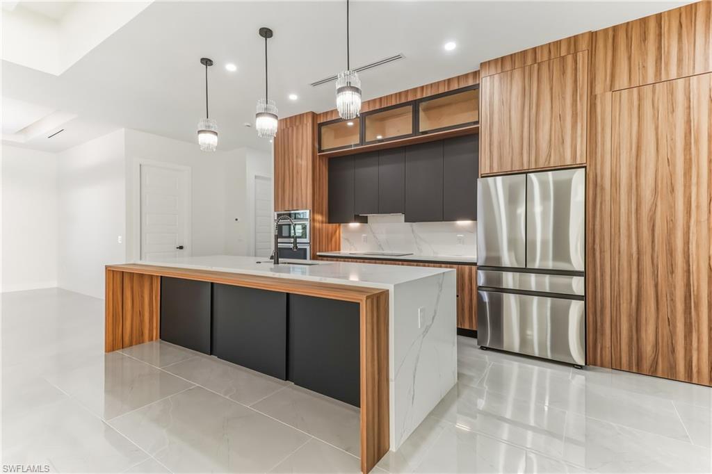 Two tone kitchen featuring dual tone cabinetry, modern cabinets, stainless steel appliances, a center island with sink, and decorative light fixtures