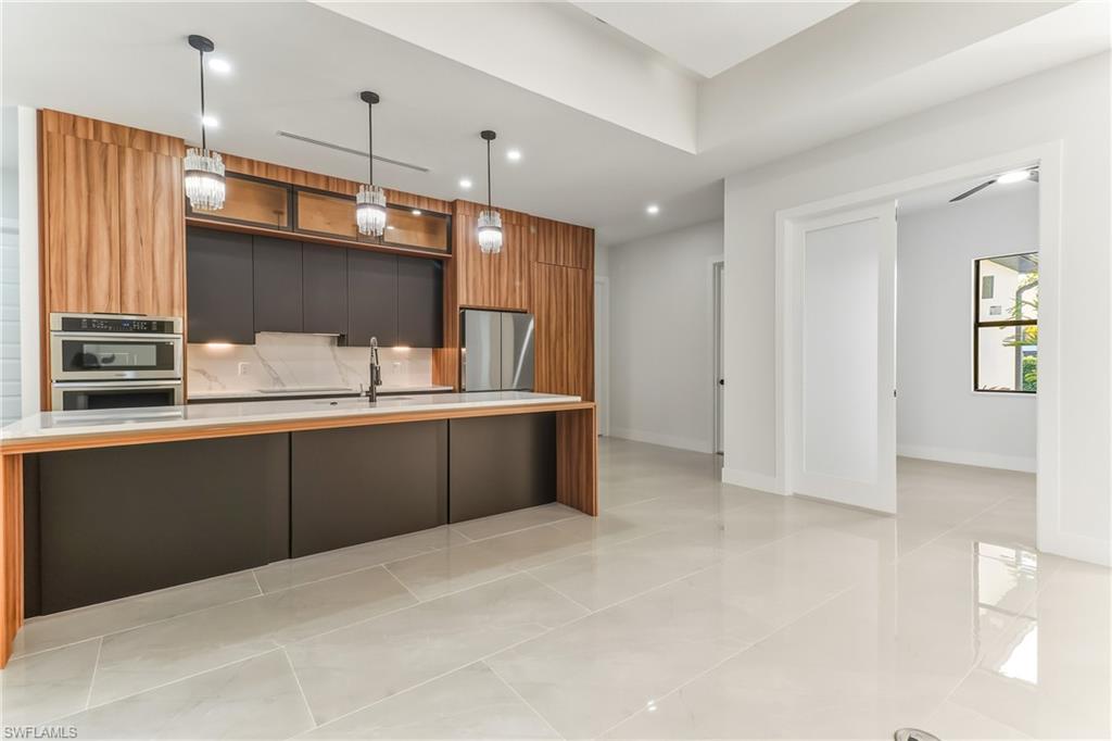 Kitchen with modern cabinets, a large icenter sland with sink, stainless steel appliances, two tone color scheme, and hanging light fixtures