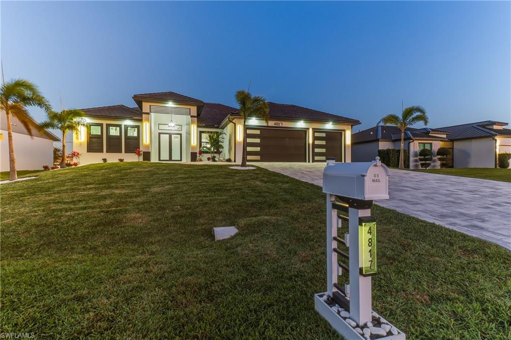 View of front facade with a front yard, decorative driveway, a 3 car garage at twilight sunset