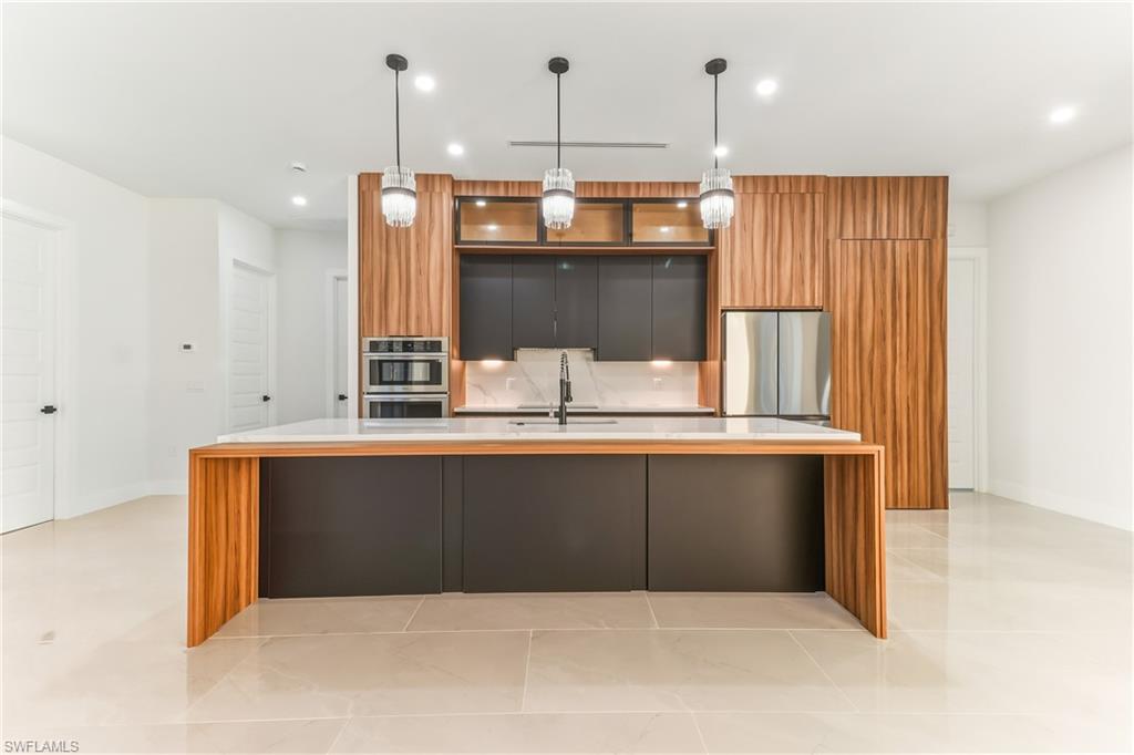 Two tone kitchen featuring modern cabinets, dual tone cabinets, a large island, light quartz countertops, and pendant lighting
