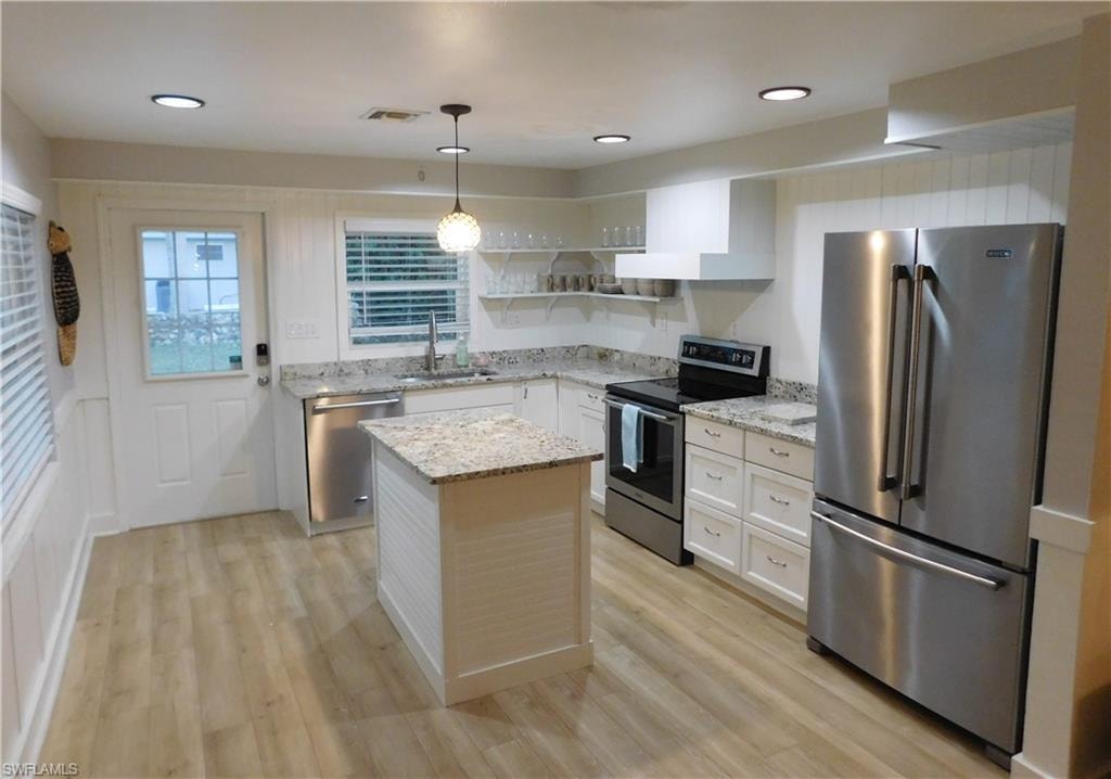 Kitchen with stainless steel appliances, white cabinets, open shelves, decorative light fixtures, and light stone countertops