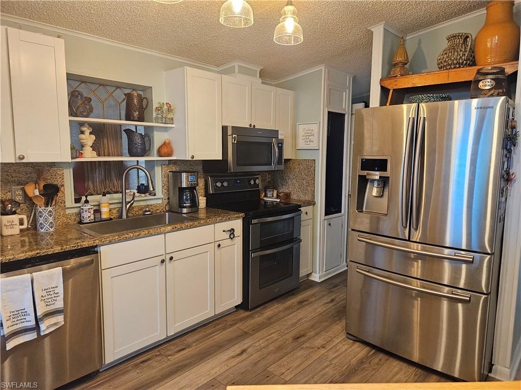 Kitchen with dark countertops, a sink, white cabinets, stainless steel appliances, and open shelves