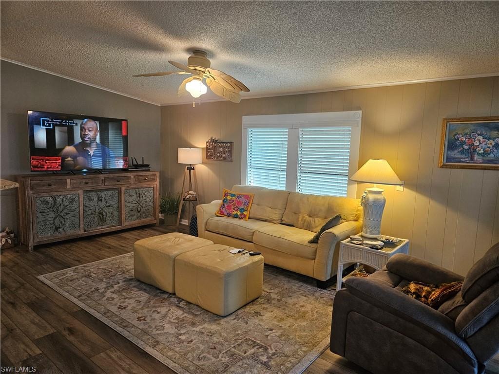 Living room with ceiling fan, a textured ceiling, wood finished floors, and ornamental molding