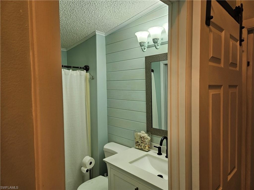 Bathroom featuring wood walls, vanity, toilet, crown molding, and a textured ceiling