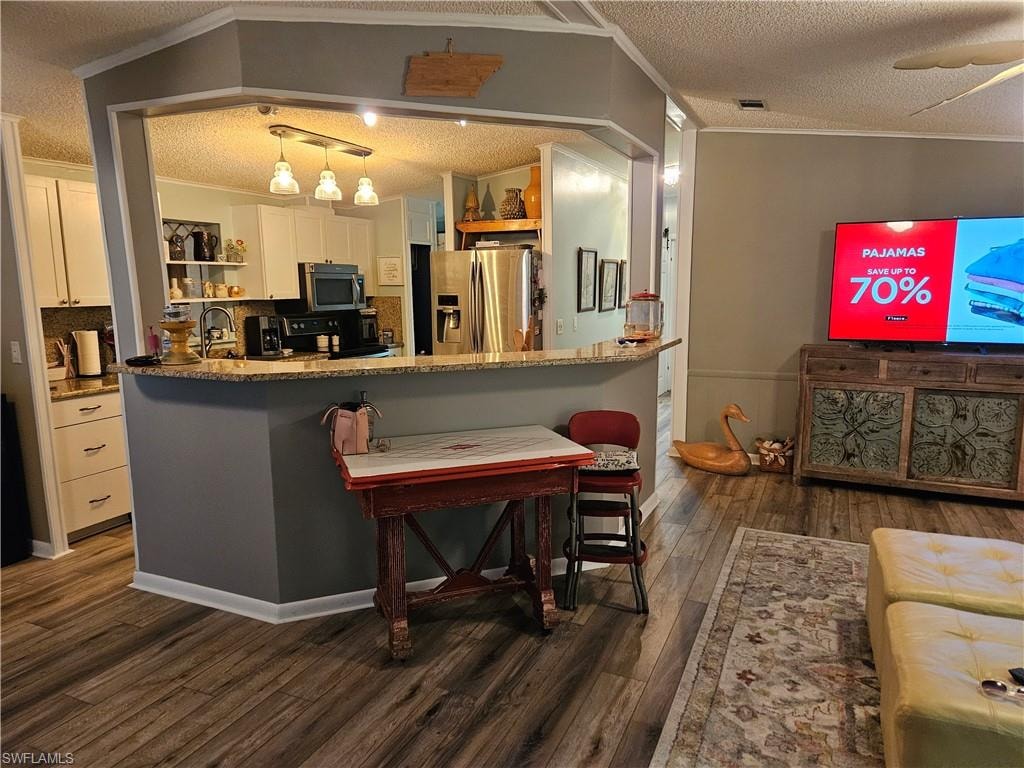 Kitchen with white cabinetry, hanging light fixtures, stainless steel appliances, and a kitchen bar