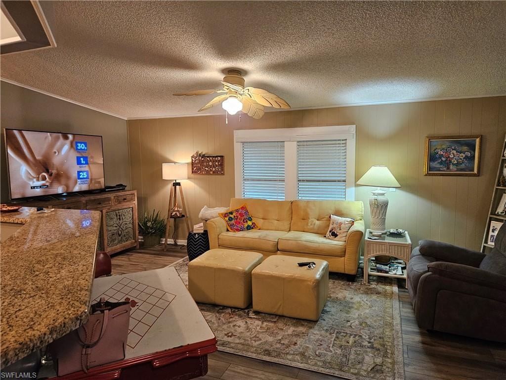 Living room with crown molding, ceiling fan, dark hardwood / wood-style flooring, and a textured ceiling