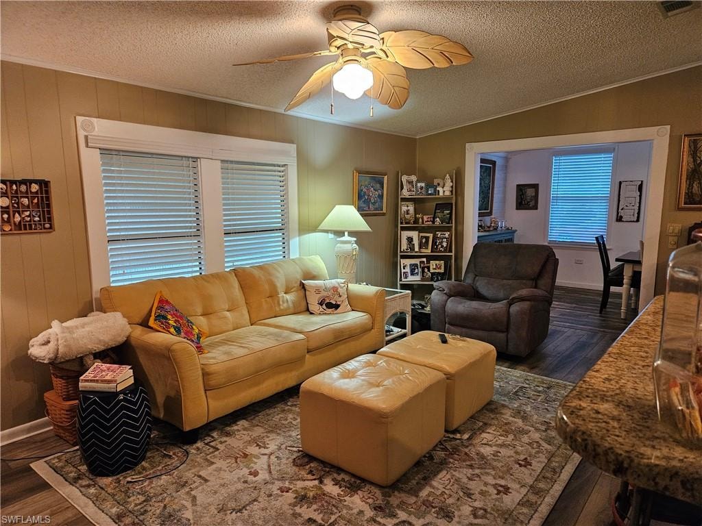 Living room featuring dark hardwood / wood-style flooring, ceiling fan, ornamental molding, and a textured ceiling