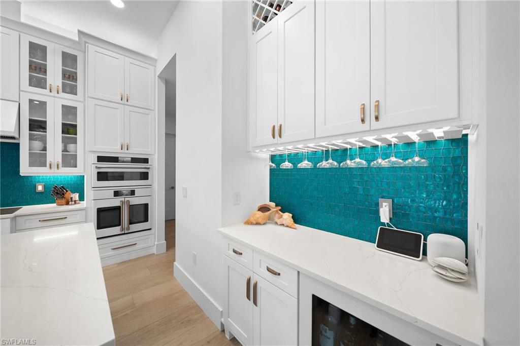 Kitchen with white cabinets, light stone counters, backsplash, glass insert cabinets, and recessed lighting