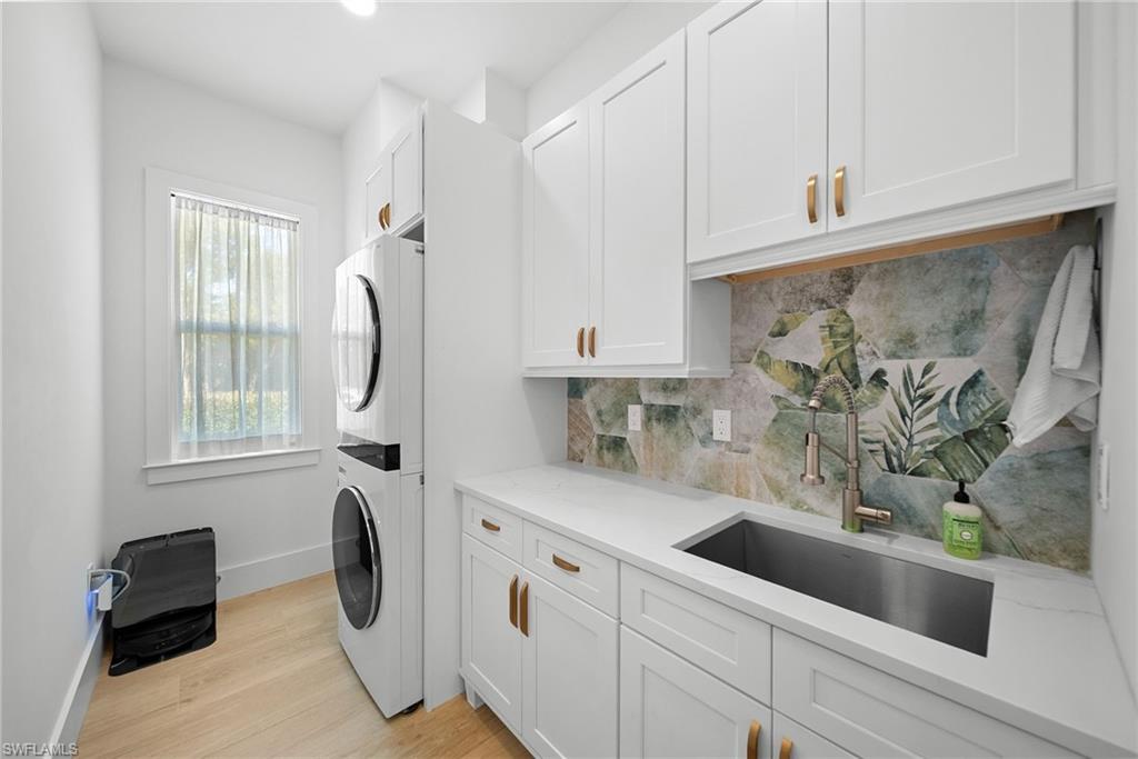 Laundry room with stacked washer / dryer, light wood-style floors, and cabinet space