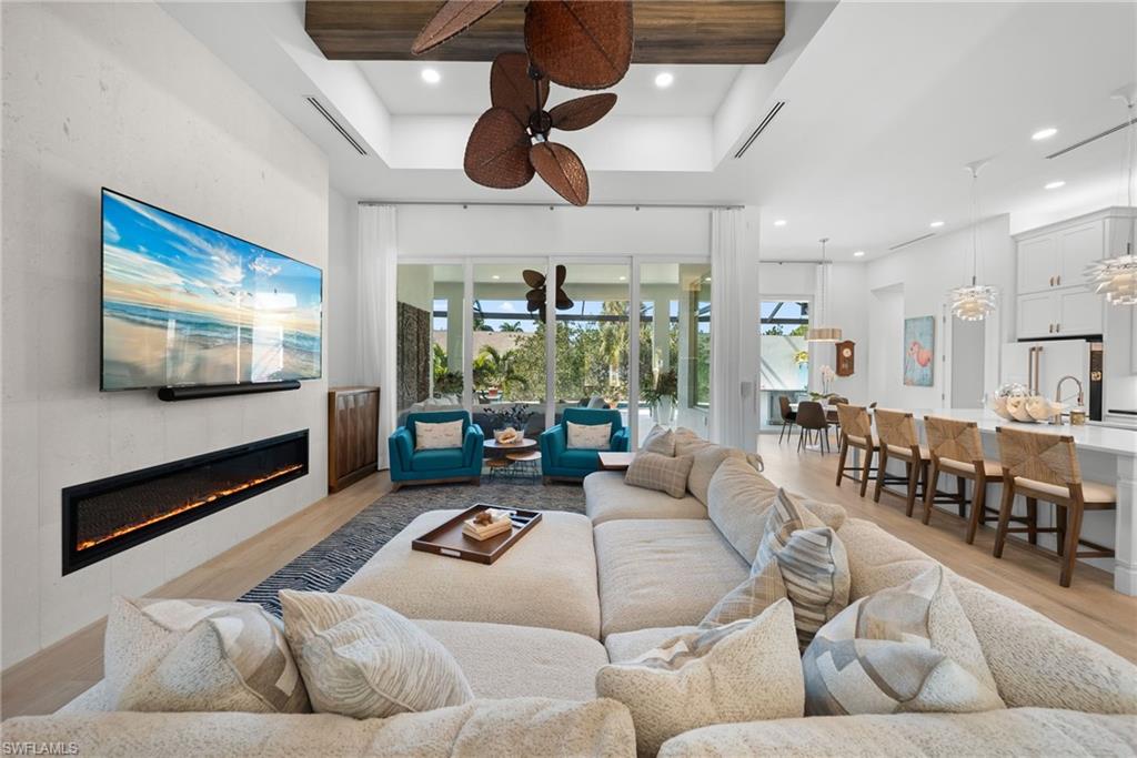 Living room featuring light wood-type flooring, a tiled fireplace, a high ceiling, a ceiling fan, and recessed lighting