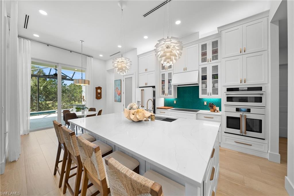 Kitchen with glass insert cabinets, white cabinetry, hanging light fixtures, light stone counters, and a breakfast bar