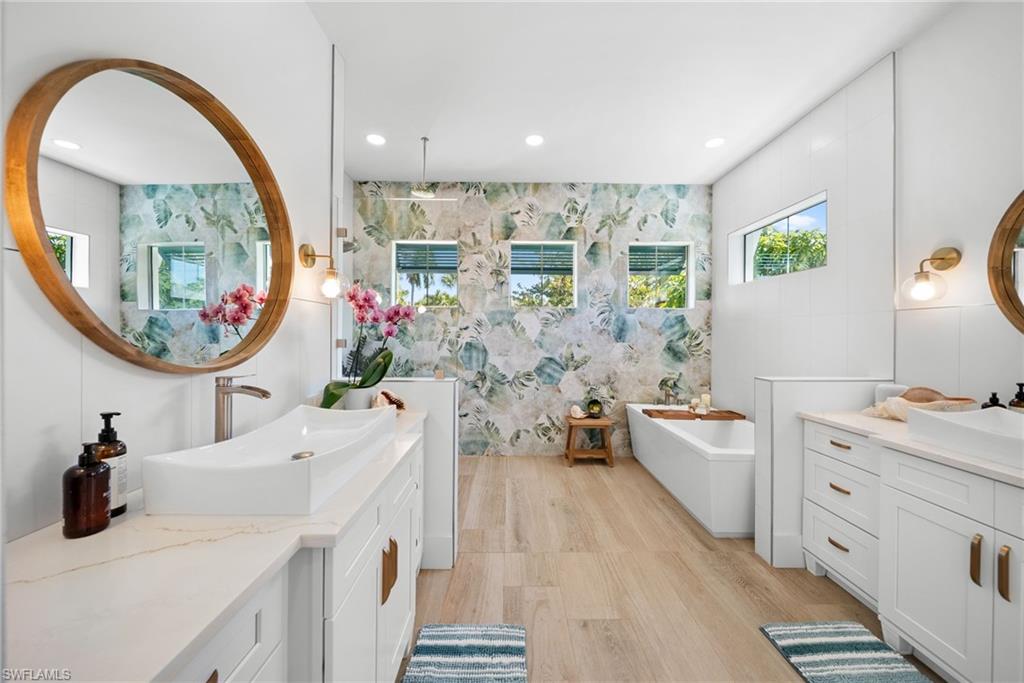 Bathroom with two vanities, a freestanding bath, recessed lighting, and light wood-style floors