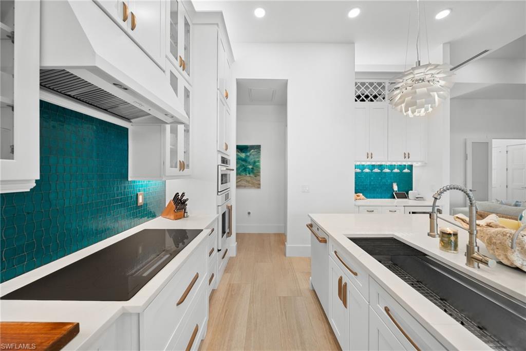 Kitchen with glass insert cabinets, white cabinets, light wood finished floors, and black electric cooktop