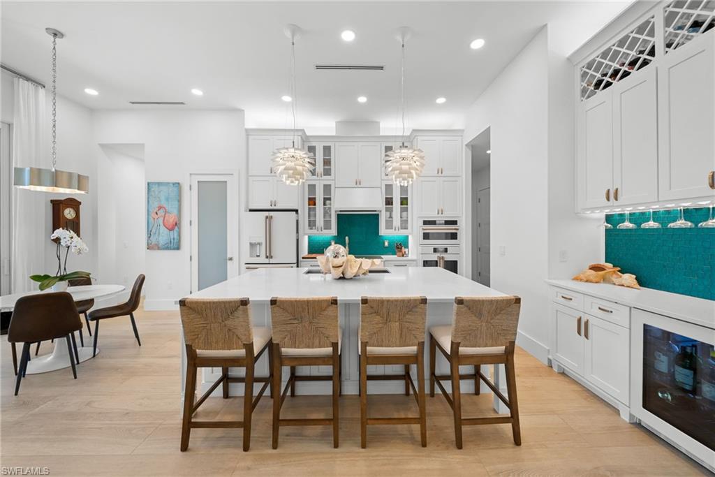 Kitchen featuring glass fronted cabinets, wine cooler, pendant lighting, light wood-style floors, and white cabinetry