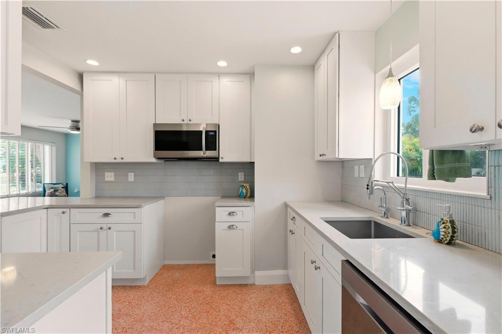 Kitchen featuring white cabinets, stainless steel appliances, decorative light fixtures, light stone countertops, and tasteful backsplash