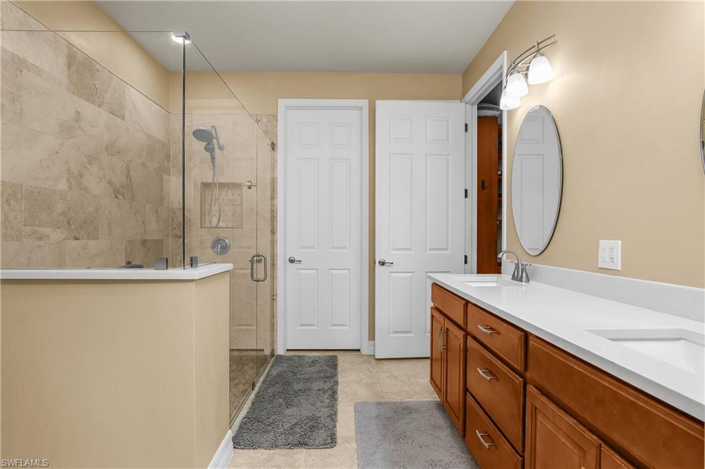 Full bathroom featuring a shower stall, double vanity, and light tile patterned floors
