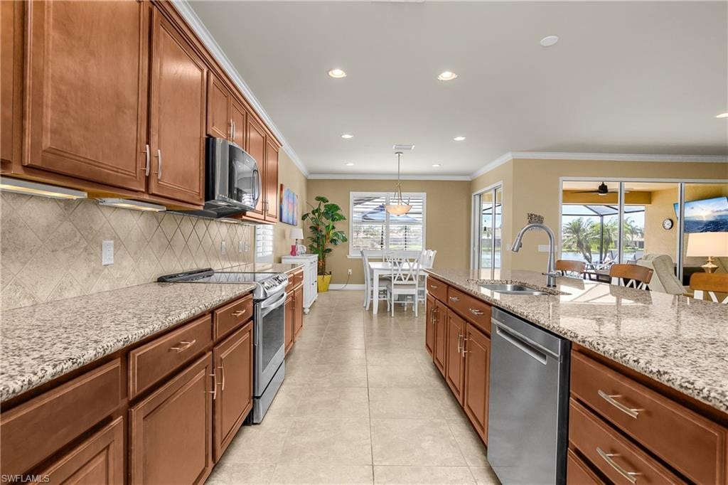 Kitchen featuring stainless steel appliances, light stone countertops, wood finish cabinetry, decorative light fixtures, and light tile patterned floors