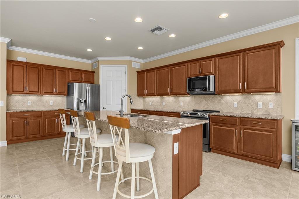 Kitchen featuring wood finish cabinetry, a breakfast bar, stainless steel appliances, ornamental molding, and recessed lighting