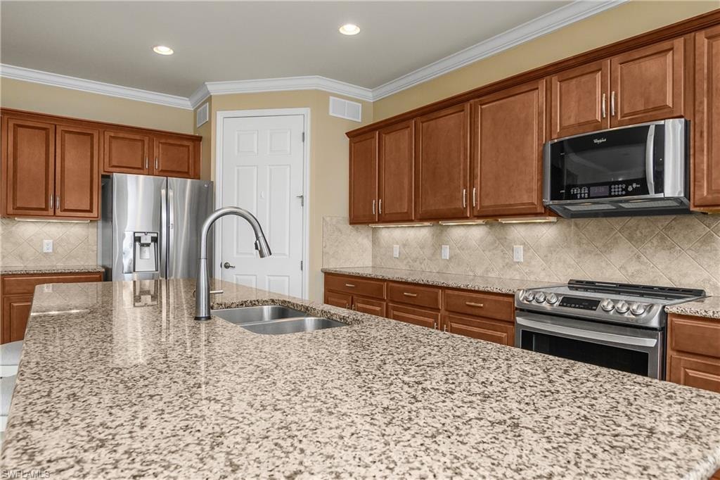 Kitchen with wood finish cabinetry, stainless steel appliances, light stone counters, ornamental molding, and tasteful backsplash