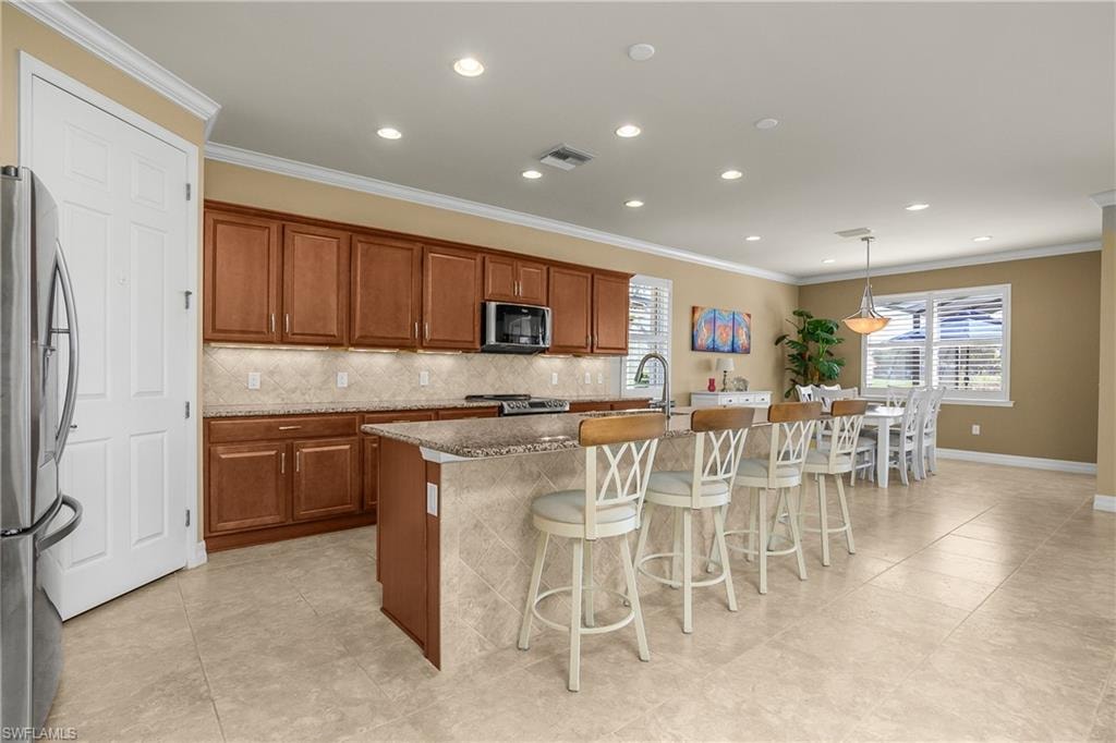 Kitchen featuring wood finish cabinetry, stainless steel appliances, a kitchen breakfast bar, backsplash, and ornamental molding