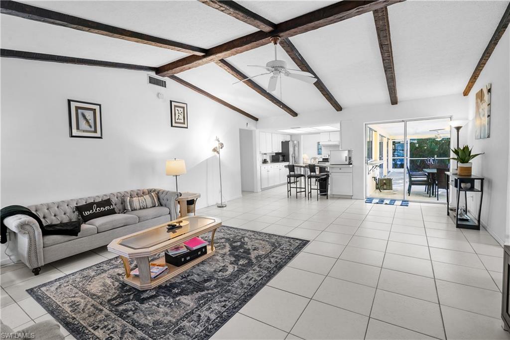 Living room with light colored large tile  large floors and high valuted ceiling and a celiling fan. Enterance to the guest wing and laundry room are off the family room.