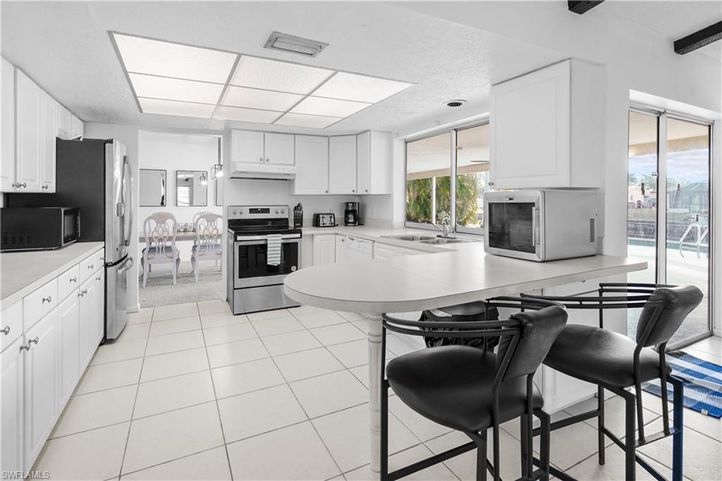 Kitchen featuring open floor plan, white cabinetry, a peninsula, light countertops, and stainless steel wine cooler.