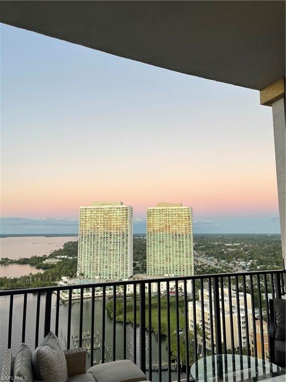 Balcony at dusk featuring a water view and a city view