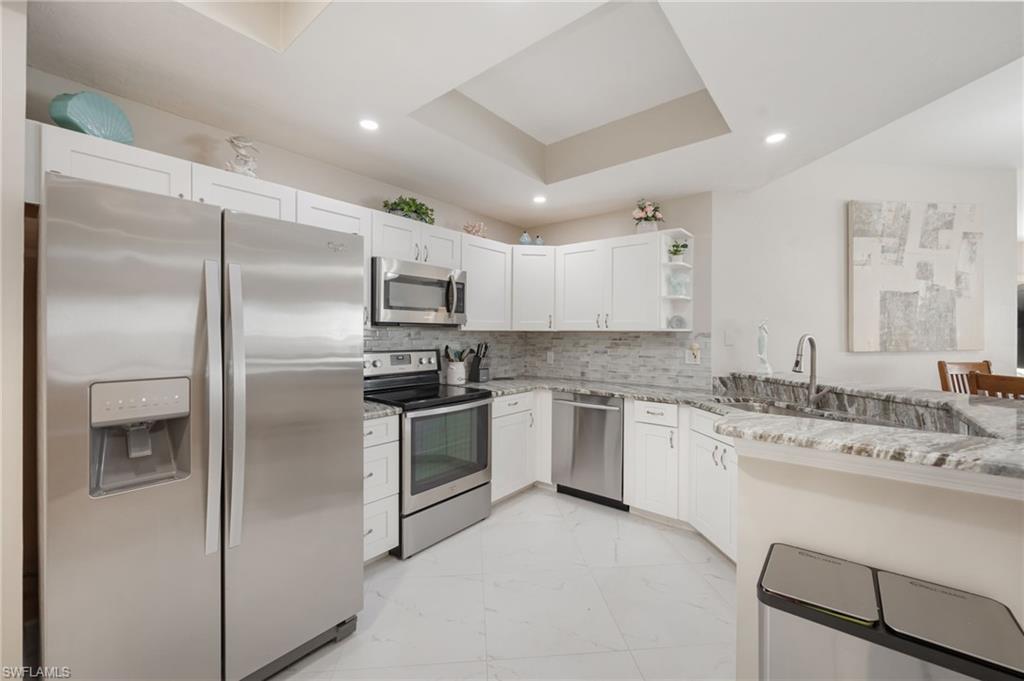Kitchen with stainless steel appliances, open shelves, a tray ceiling, light stone counters, and backsplash