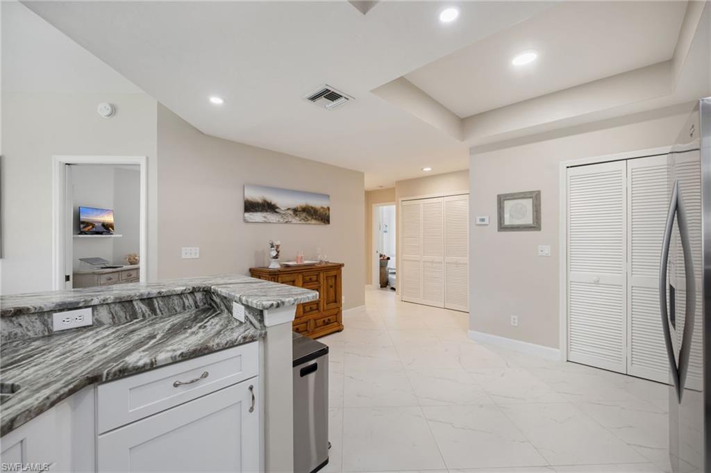 Kitchen with stainless steel fridge, white cabinetry, dark stone countertops, light marble finish floors, and recessed lighting