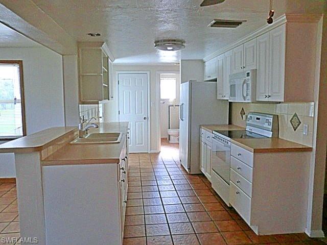 Kitchen with white appliances, light countertops, white cabinets, a textured ceiling, and a peninsula