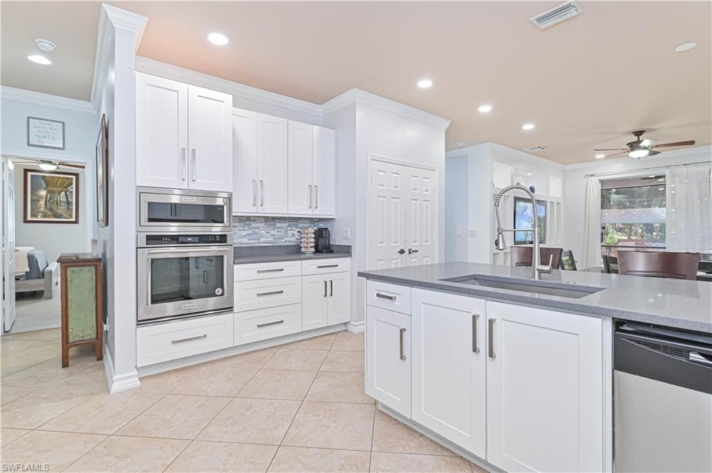 Kitchen with white cabinetry, a ceiling fan, stainless steel appliances, dark stone counters, and ornamental molding