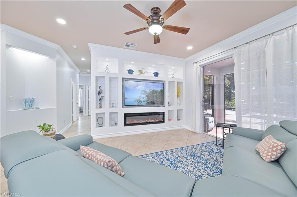 Living area with ceiling fan, ornamental molding, a glass covered fireplace, light tile patterned floors, and recessed lighting