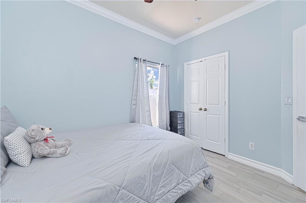 Bedroom with light wood-style flooring, crown molding, a closet, and ceiling fan
