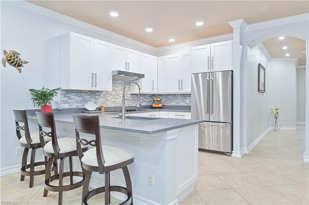 Kitchen with arched walkways, ornamental molding, white cabinets, high end refrigerator, and backsplash